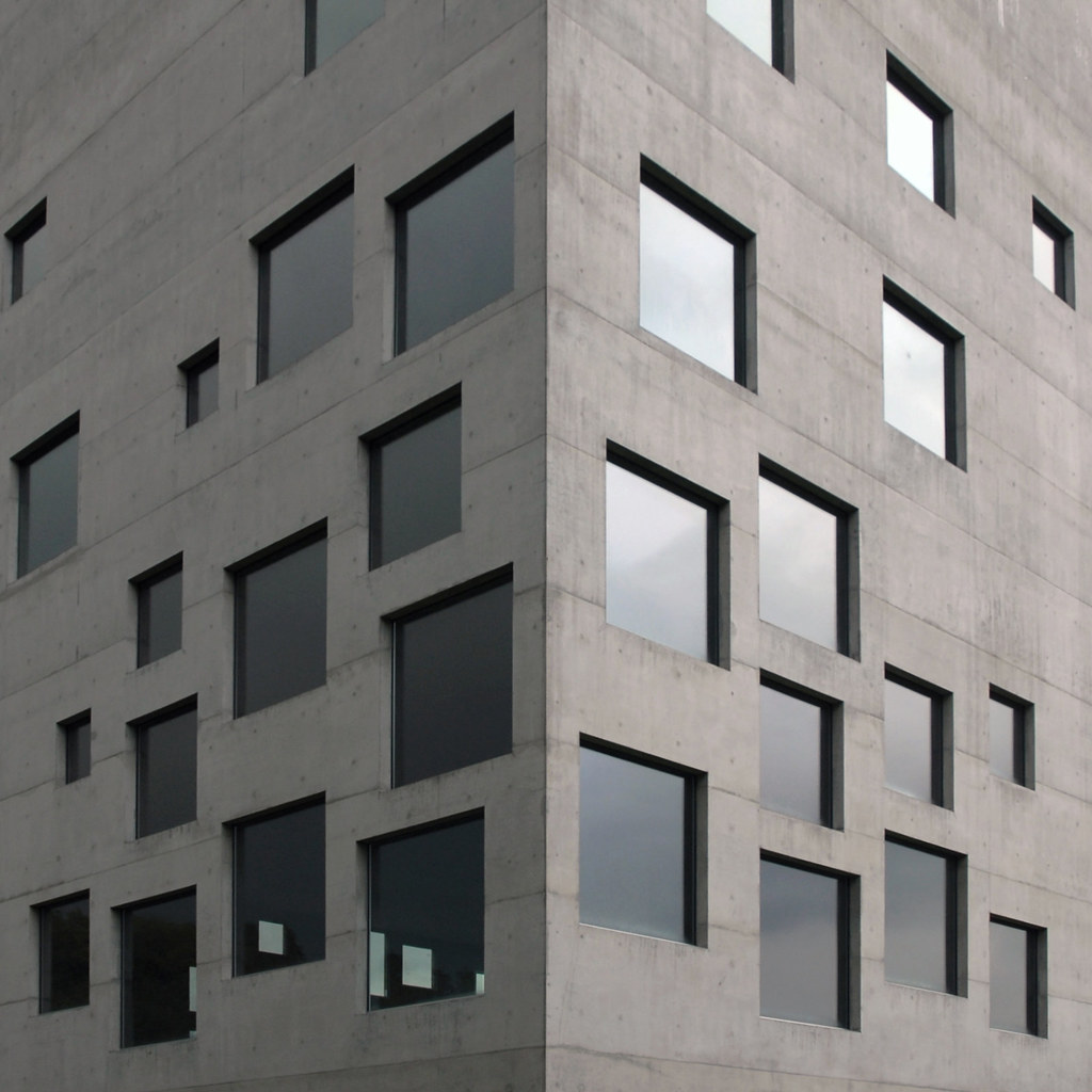Concrete office building corner with rows of windows under an overcast sky