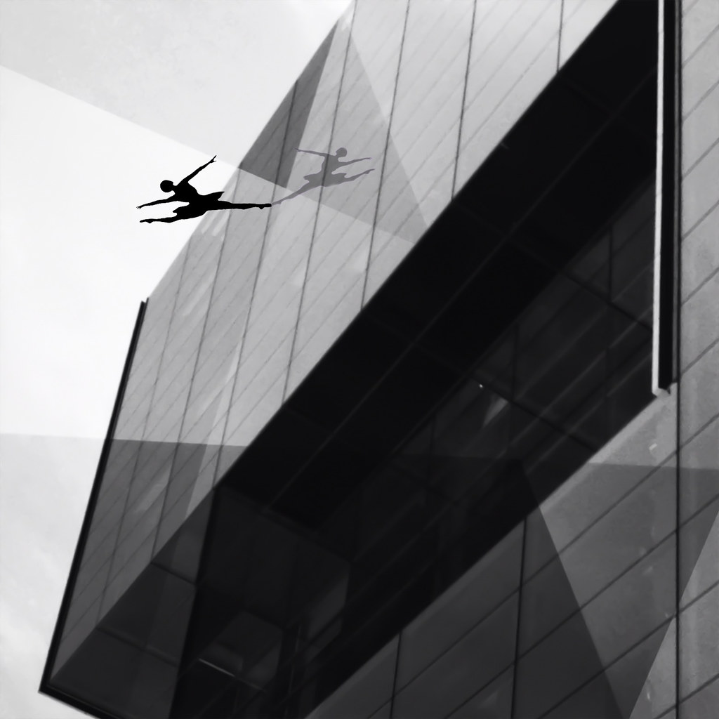 Silhouette of a dancer leaping in front of a glass office building